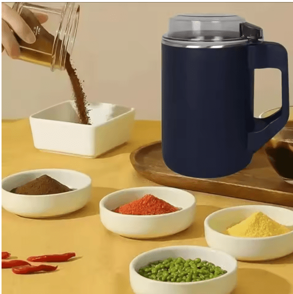 Navy electric coffee grinder with clear lid and handle beside ground spices