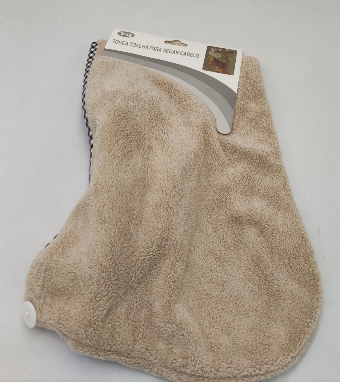Beige hair drying cap towel with a hanging loop and white fastening button.
