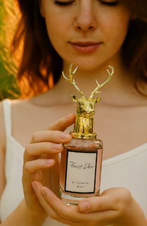 Forest Deer perfume in a clear bottle with a gold deer-head cap, held in both hands.