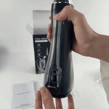 Black oral irrigator with a clear water tank, held upright in a hand